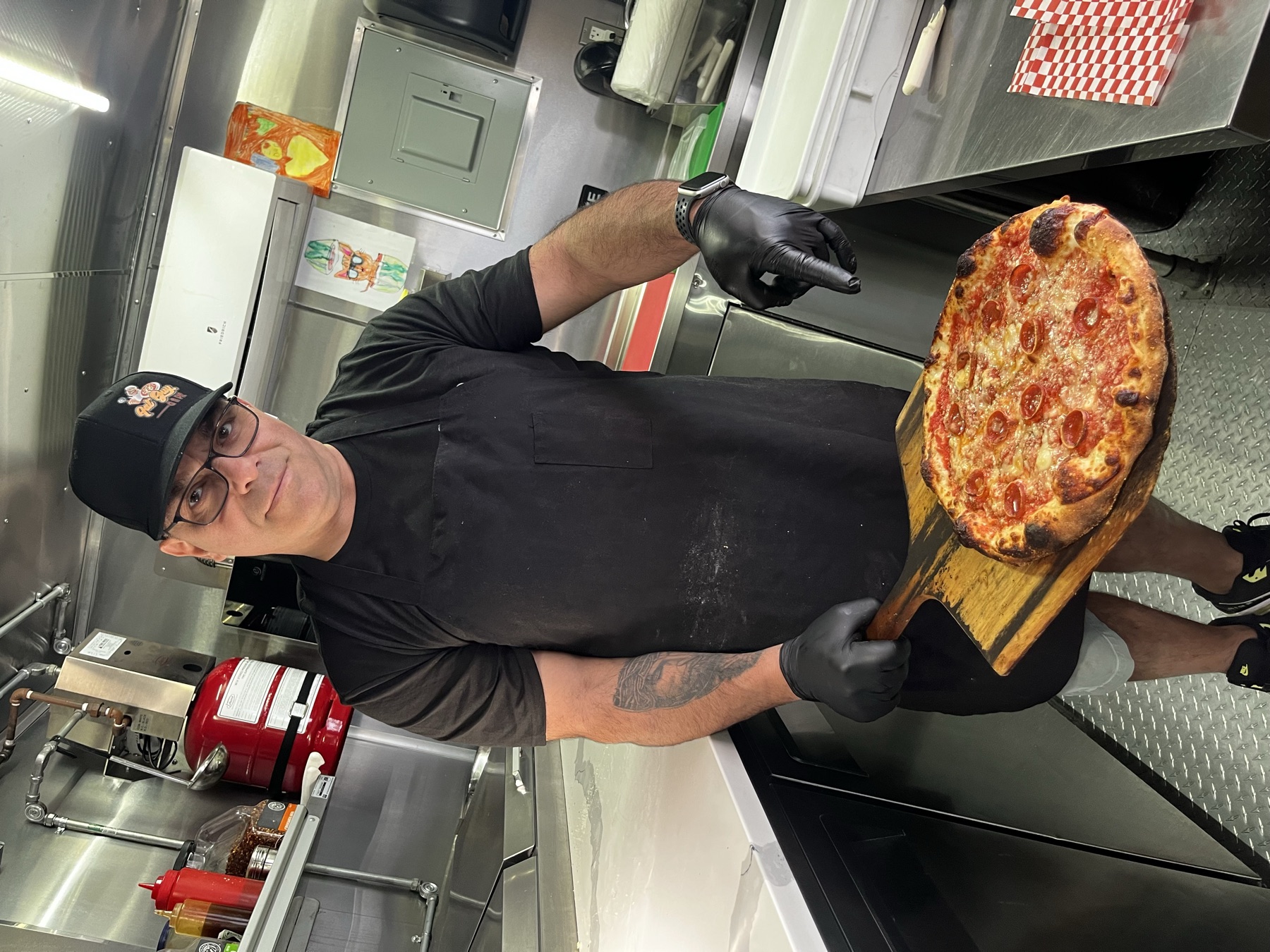 Founder of Fat Guy And A Pie of New York holding a freshly baked pizza inside the food truck